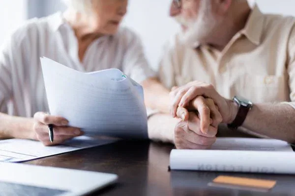 Cropped view of senior couple holding hands near documents, laptop and credit card on table